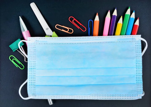 Siyah arka planda okul eşyaları ve virüs koruyucu maske. Üst görünüm