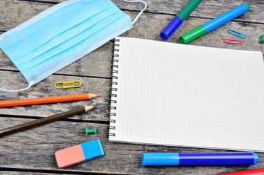 Masasında yüz maskesi ve okul aletleri olan boş bir defter
