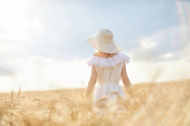 gündüz sırasında buğday alanında yükseltilmiş kollar ile şapkalı beyaz kadın