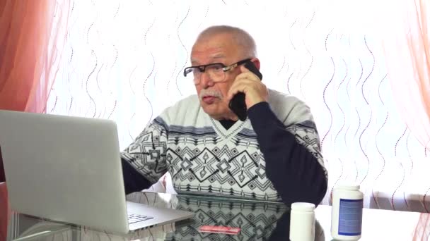 Hombre mayor habla en el teléfono negro y tipos en el ordenador portátil — Vídeo de stock