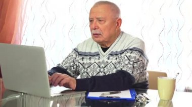 gri saçlı kıdemli adam bilgisayarda çalışır ve çay içecekler