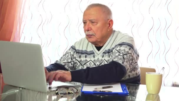 Senior man texts information in laptop and drinks tea — Stock Video