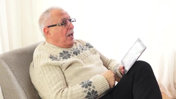 Hombre mayor en suéter blanco navega por internet y sonríe — Vídeos de Stock