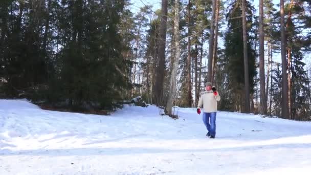 Человек в серой шляпе и синих джинсах ходит по снегу, держа лыжи — стоковое видео