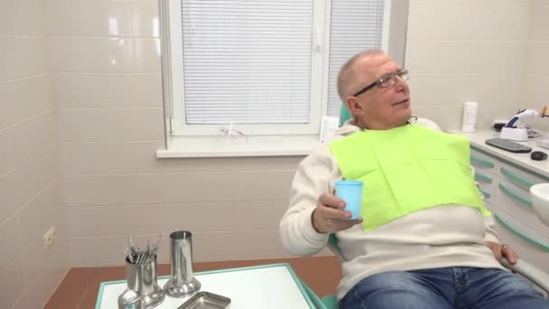 Homem senta-se no armário do dentista bebe xícara de água doce — Vídeo de Stock