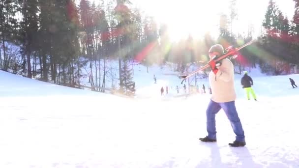 Трезвенный мужчина поднимается по канатам, неся лыжи против вечернего солнца — стоковое видео