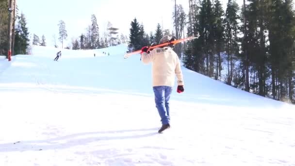 穿蓝色牛仔裤的老人肩上拿着滑雪板上山 — 图库视频影像