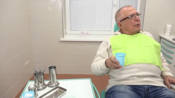 man rinses mouth with water spits sitting in dental chair