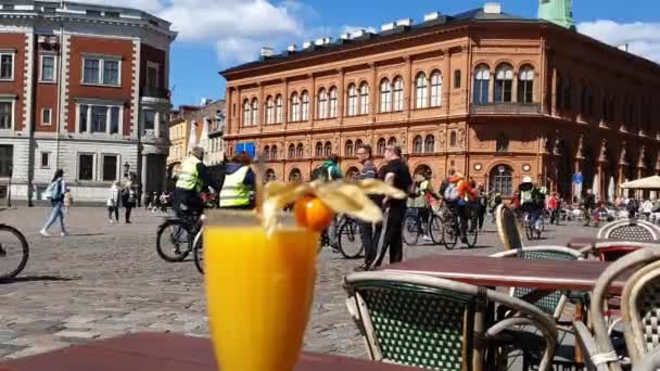 Pessoas andam de bicicleta ao longo da praça contra o edifício marrom — Vídeo de Stock