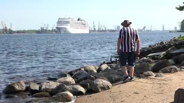 Muž chodí na řece Daugava břeh sleduje velkou výletní loď — Stock video