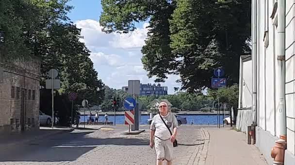 Мужчина идет по мощеной брусчаткой улице по удивительной реке — стоковое видео