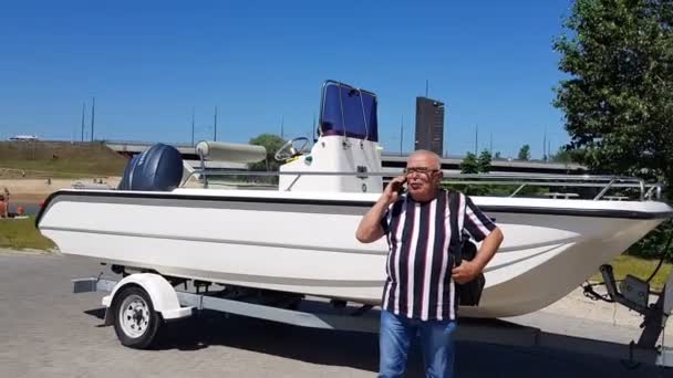 Senior man in t-shirt talks on mobile phone at motor boat — Stock Video