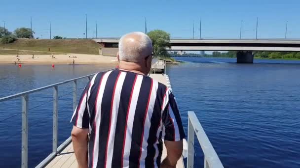 Людина з телефоном спирається на поручні на річці проти мосту — стокове відео