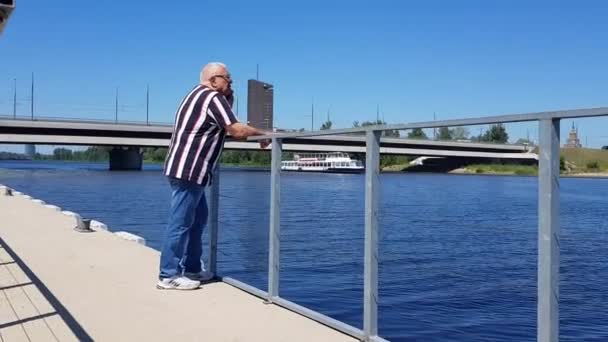 Зрілий чоловік зі смартфоном стоїть на новому пірсі влітку — стокове відео