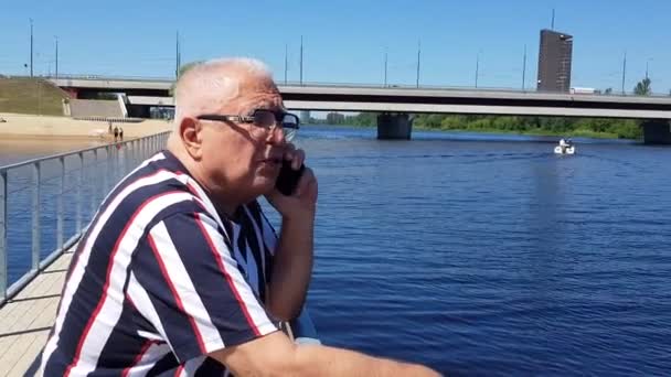 Pensionerad man talar på mobiltelefon vid vacker sommar flod — Stockvideo