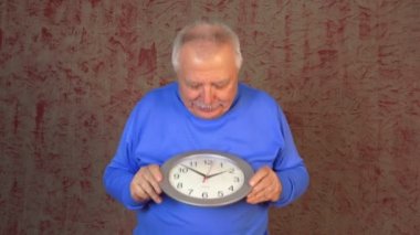 yaşlı adam modern gümüş duvar saat tutar görünüyor ve üzgün alır