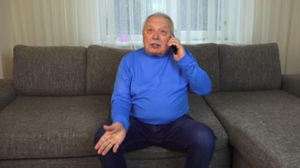 Man sitter på brun soffa rymmer svart mobiltelefon och pratar — Stockvideo