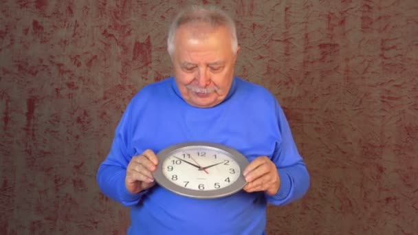 Старик с седыми волосами держит часы и показывает крутой знак — стоковое видео