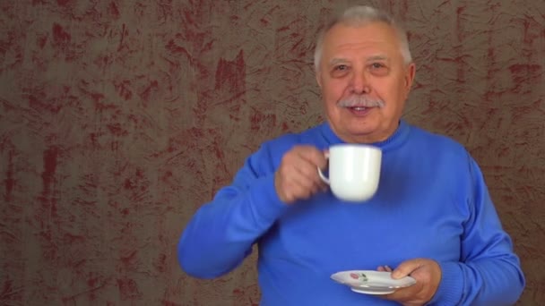 Зрілий чоловік тримає чашку з тарілкою і насолоджується зеленим чаєм — стокове відео