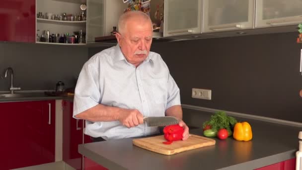 Senior man snijdt grote rode paprika met groot mes — Stockvideo