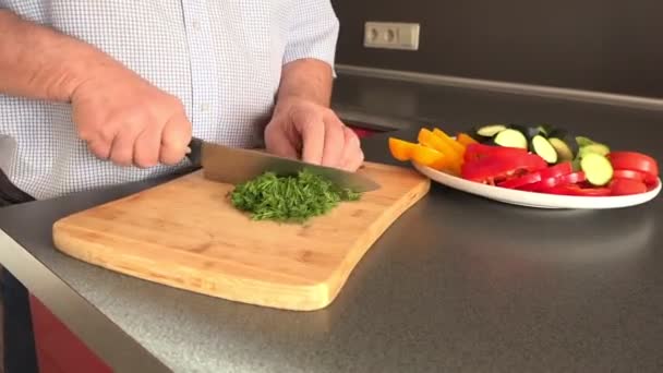 Man hand nedskärningar dill ombord nära tallrik med grönsaker — Stockvideo