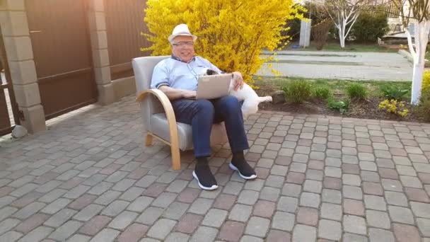 Senior man met hond types op laptop bij Bush met gele bloemen — Stockvideo