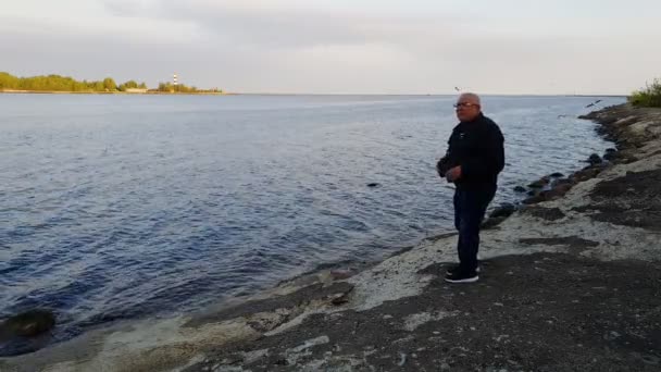 Homem caminha na margem do rio azul e fica com binóculos — Vídeo de Stock