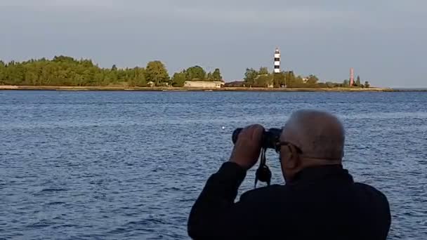 Viejo hombre tiene binocular en las manos y mira a la orilla opuesta — Vídeo de stock