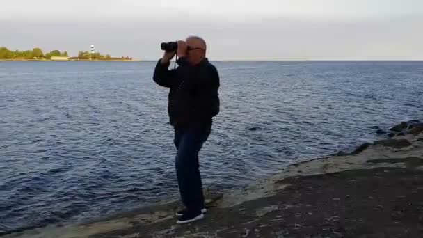남자는 돌에 서서 강에서 쌍안경을 통해 보인다 — 비디오