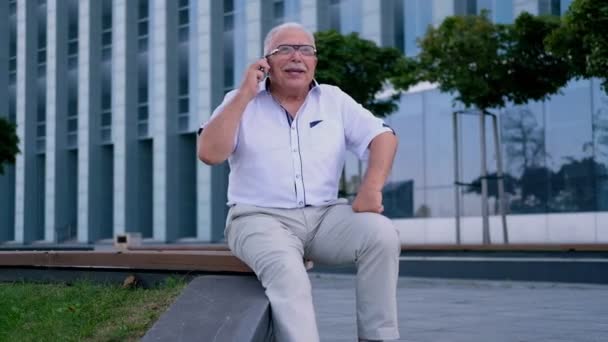 Hombre mayor habla en el teléfono celular en la calle en el edificio de oficinas — Vídeo de stock