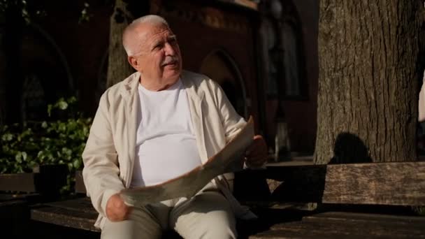 Senior man in Casual kleding met kaart kijkt rond in Park — Stockvideo