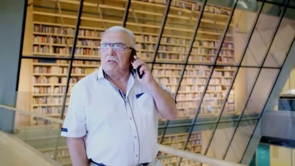 Mature intelligent man praat op mobiele telefoon in openbare bibliotheek — Stockvideo