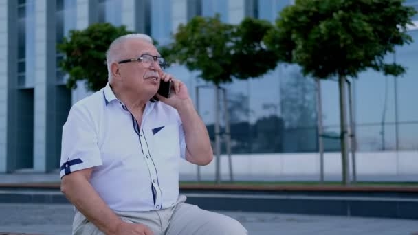 Пенсіонер має розмову на смартфоні на міській вулиці — стокове відео