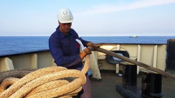 Skilled seaman folds large yellow rope against blue sea — Stock Video