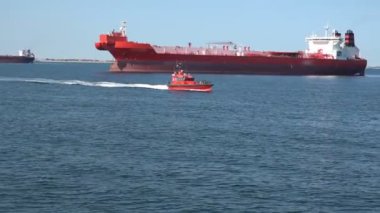 Küçük pilot motorlu gemi büyük kırmızı tankerlere karşı hızla yol alıyor.
