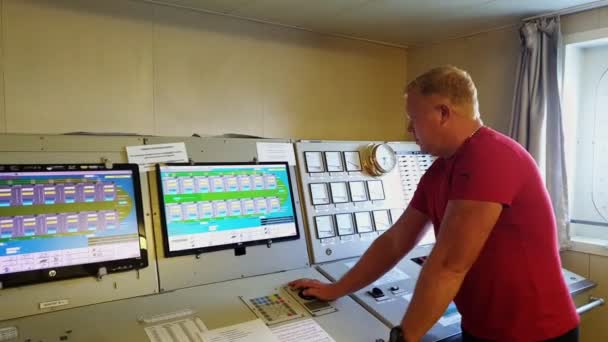 Hombre en camiseta roja se levanta cerca del panel de control con pantallas — Vídeo de stock