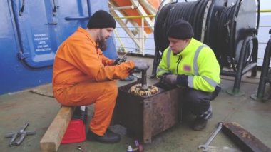 Erkekler enstrüman kullanır ve modern tanker elektrikli motoru tamir ederler.