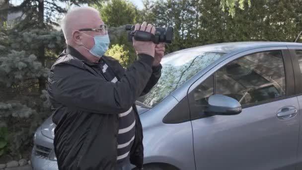 Ηλικιωμένος άνδρας με μάσκα κρατά μικρή κάμερα και τραβάει βίντεο — Αρχείο Βίντεο