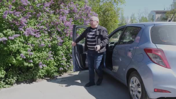 Äldre man lämnar bilen lägger handen i fickan och pratar i telefon — Stockvideo