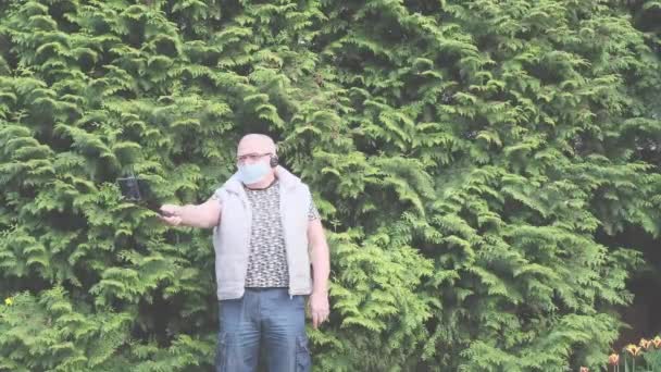 Důchodce v masce drží selfie hůl s fotoaparátem borovicemi — Stock video