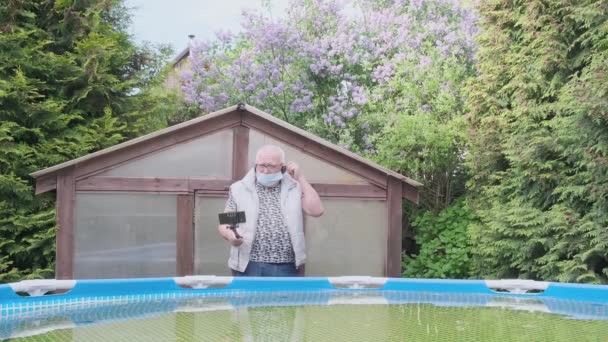 회색 머리의 남자가 시골 집 마당에서 파란색 마스크를 벗고 — 비디오
