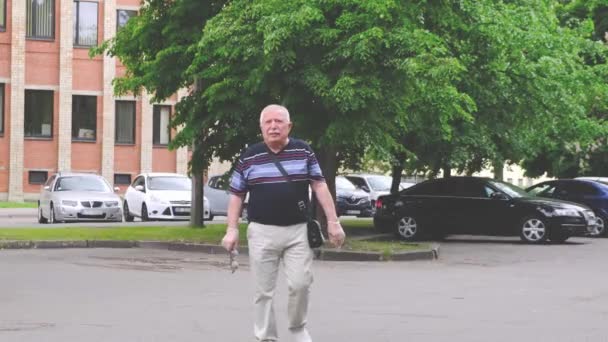 Starší muž drží brýle v ruce a jde ke kameře — Stock video