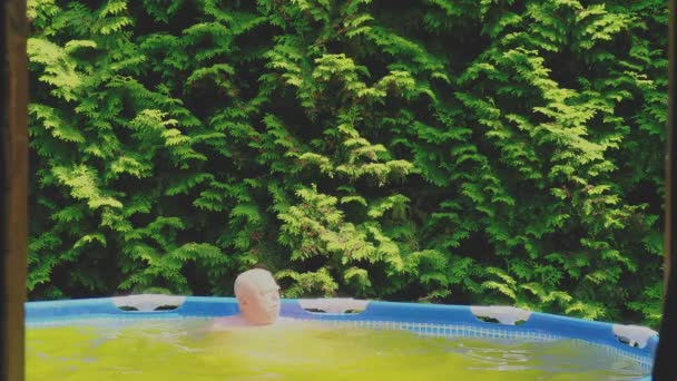 Старший мужчина с седыми усами расслабляется в надувном бассейне — стоковое видео