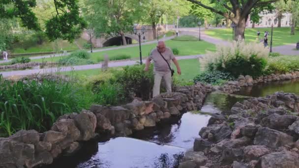 Пенсионер в очках наслаждается прогулкой по современной парковой зоне — стоковое видео