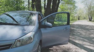 Emekli adam kapıyı açar, gri arabadan iner ve el sallar.