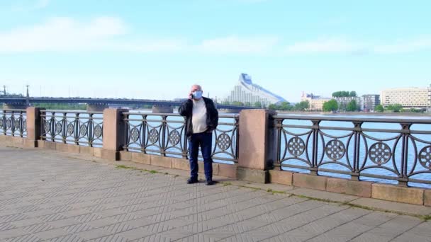 Nyugdíjas férfi maszkban és szemüvegben beszél telefonon a folyóparton — Stock videók