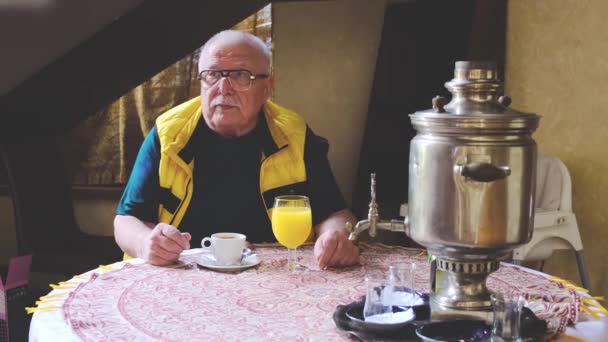 Chauve homme portant des lunettes est assis à table avec une tasse de café — Video