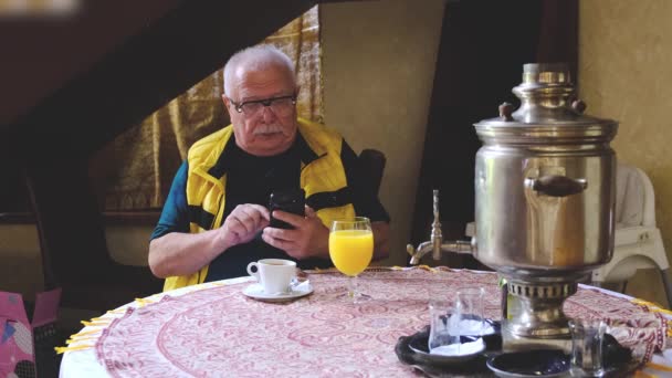 Ernstige gepensioneerde zit aan tafel en begint te praten over de telefoon — Stockvideo