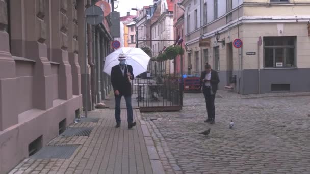 Senior mit Maske und geöffnetem Regenschirm läuft die Straße entlang — Stockvideo