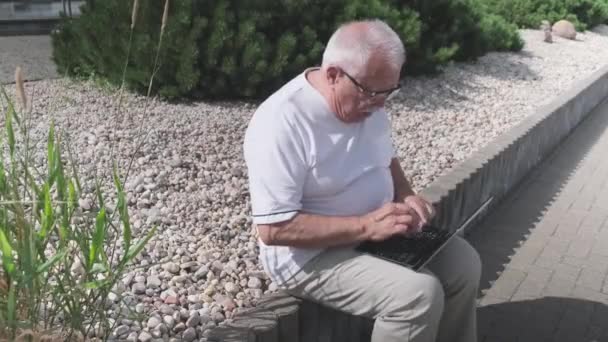 Щасливий зрілий чоловік в окулярах використовує ноутбук у міському парку — стокове відео